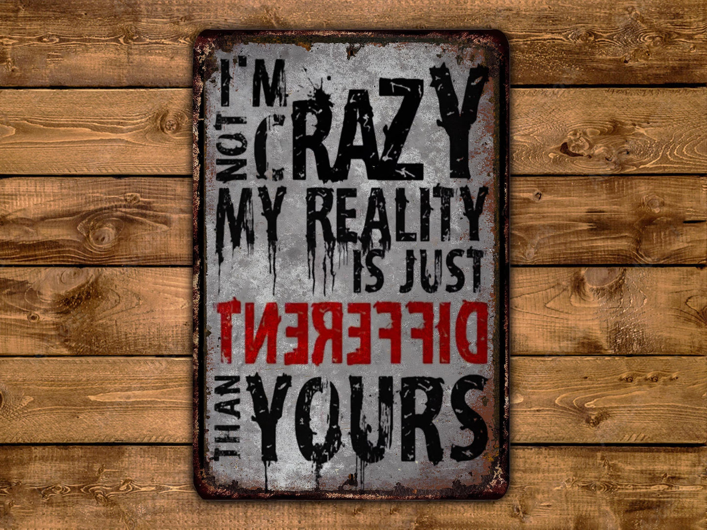 a sign with the text "I'm not crazy, my reality is just different than yours" in a distressed, distressed font against a wooden background.