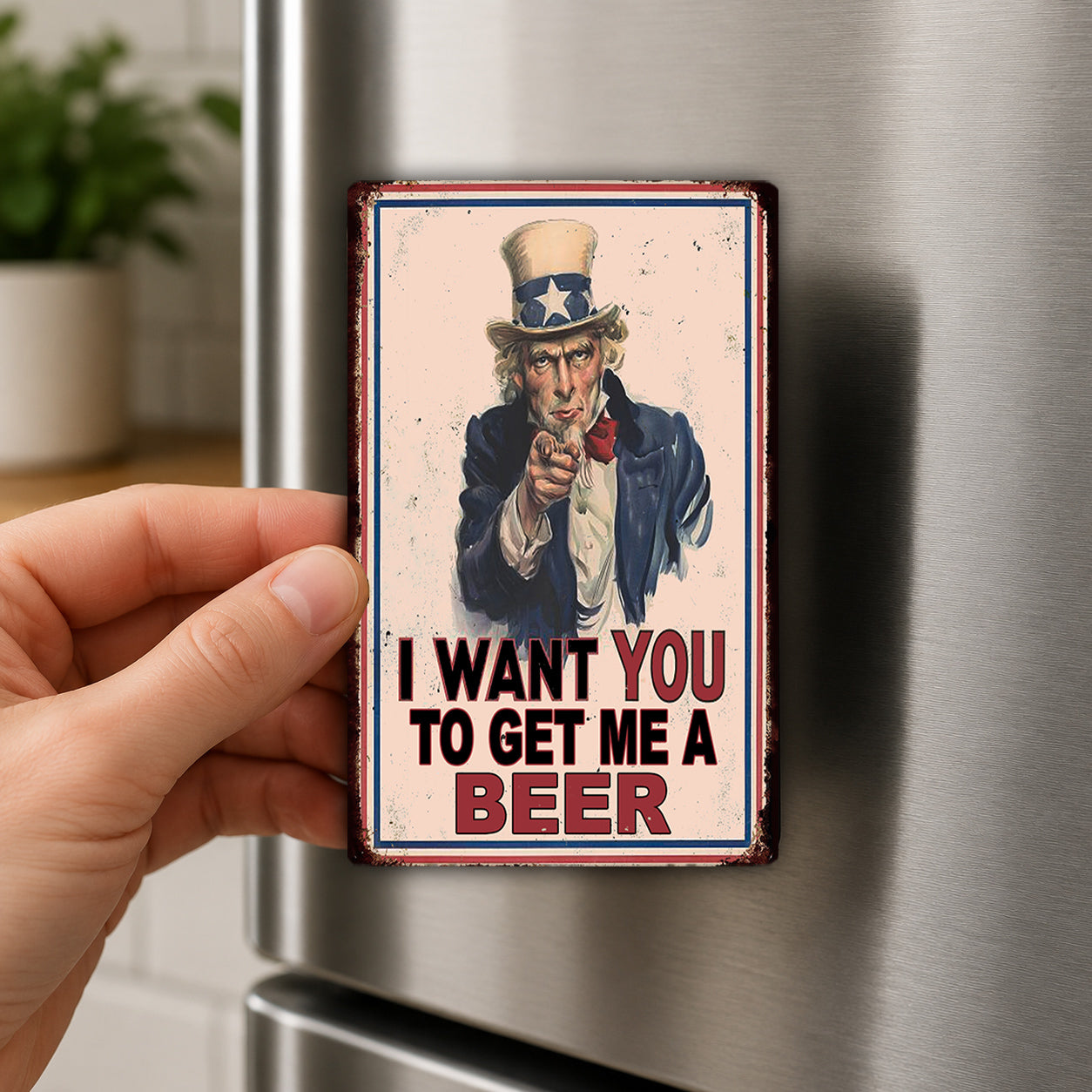 A person's hand is holding a metal magnet with a picture of Uncle Sam and the text "I WANT YOU TO GET ME A BEER" on it.