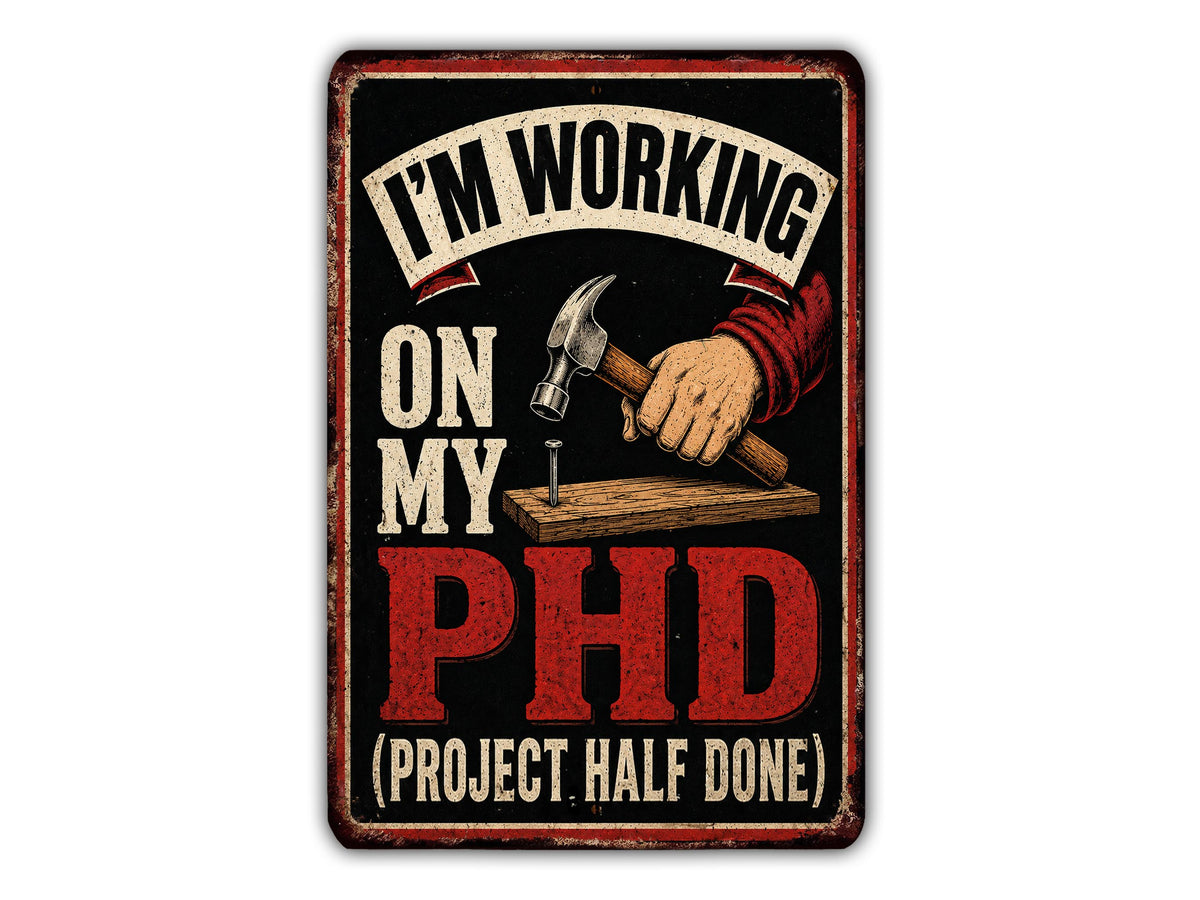 The image is a sign with the text "I'M WORKING ON MY PHD (PROJECT HALF DONE)" and an illustration of a hand holding a hammer.