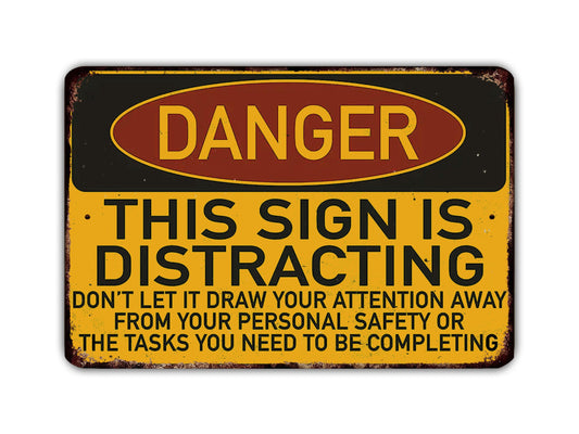 a sign with the word "DANGER" in large letters, indicating a warning or hazard. The sign also contains a message that says "THIS SIGN IS DISTRACTING" and advises not to draw attention away from personal safety or the tasks that need to be completed.