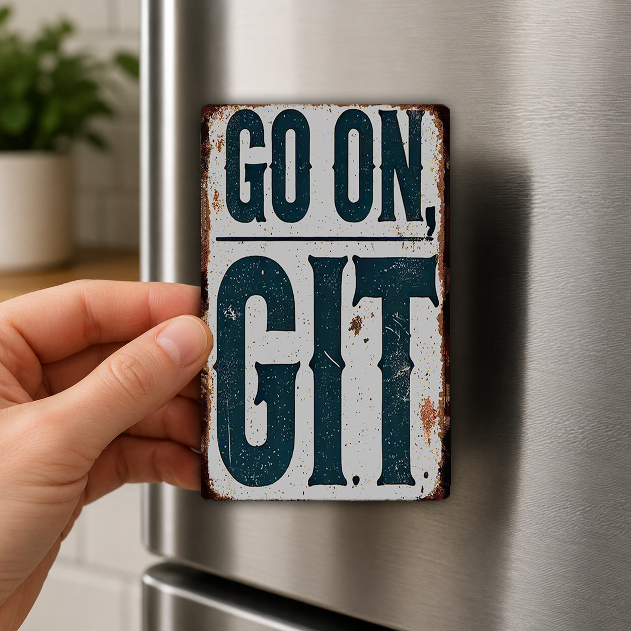 A hand is holding a metal sign with the text "GO ON GIT" on it, which is attached to a refrigerator.