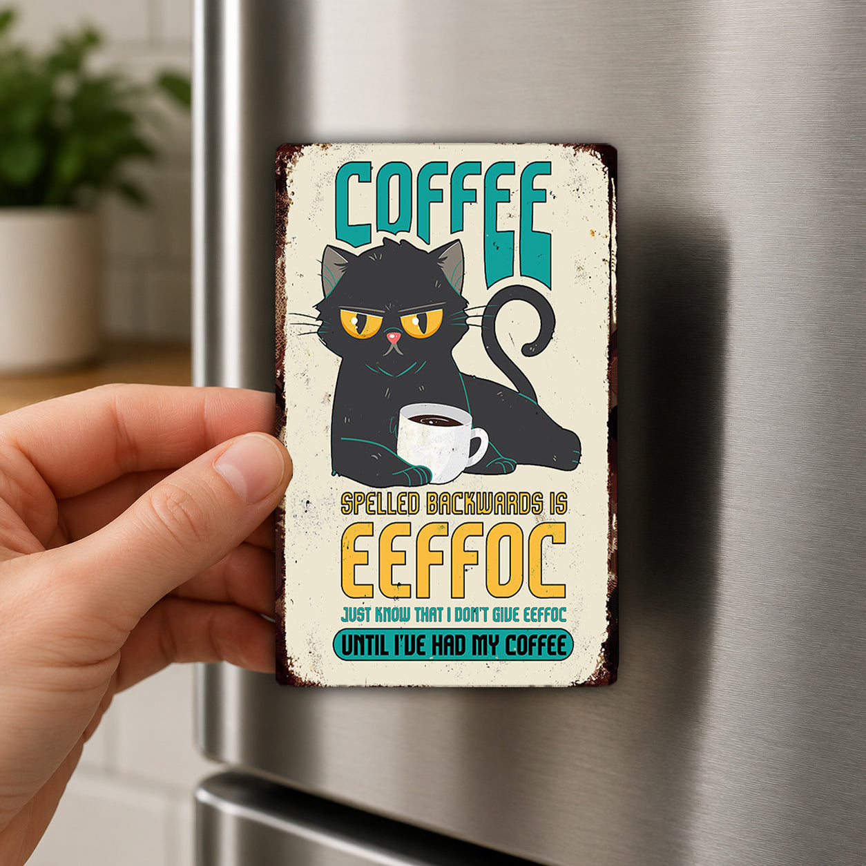 A person's hand holding a metal refrigerator magnet with a cartoon cat and text.