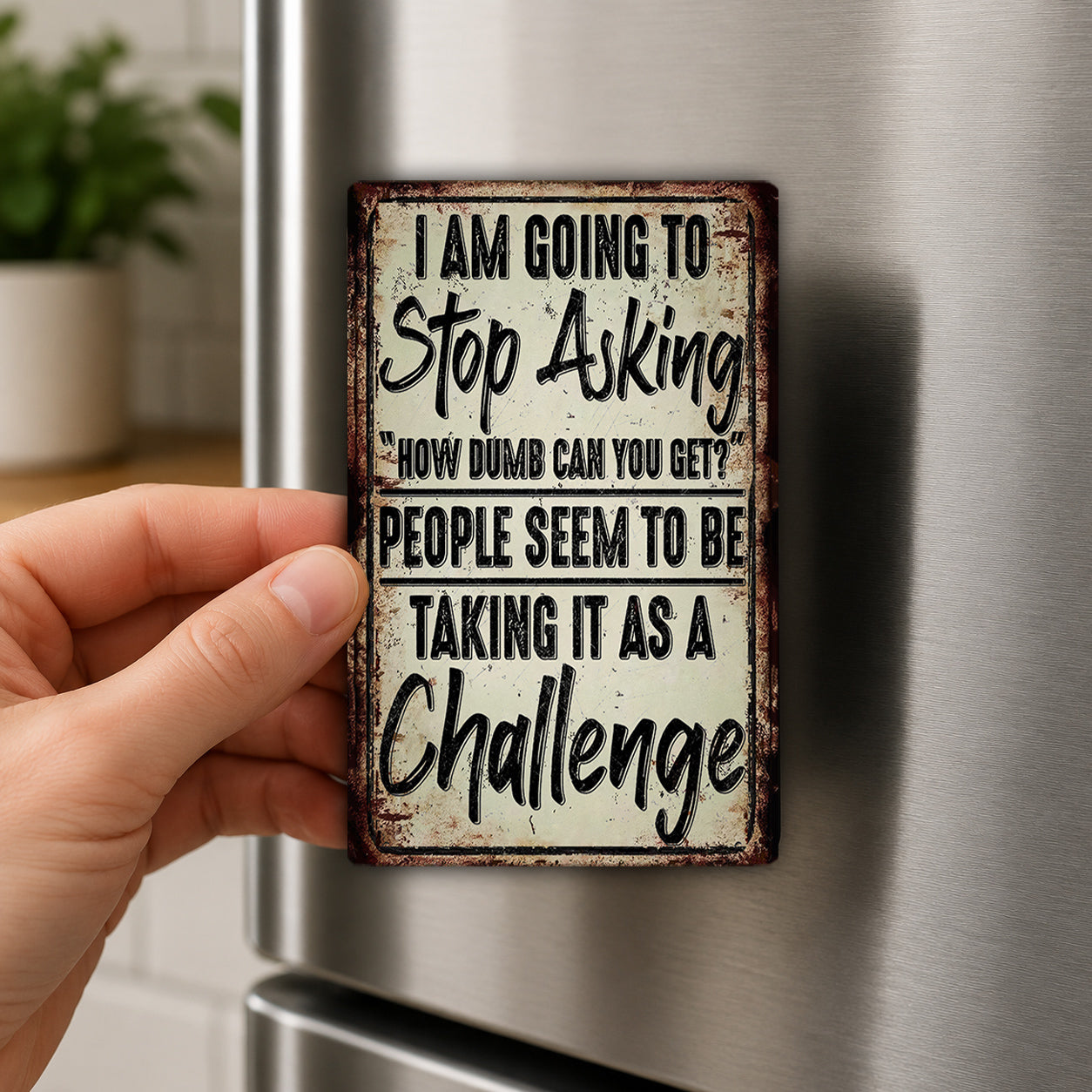 A person's hand is holding a metal sign with a humorous message on it.