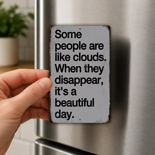 A person's hand is holding a small, rectangular magnet with a message on it, which reads "Some people are like clouds. When they disappear, it's a beautiful day."