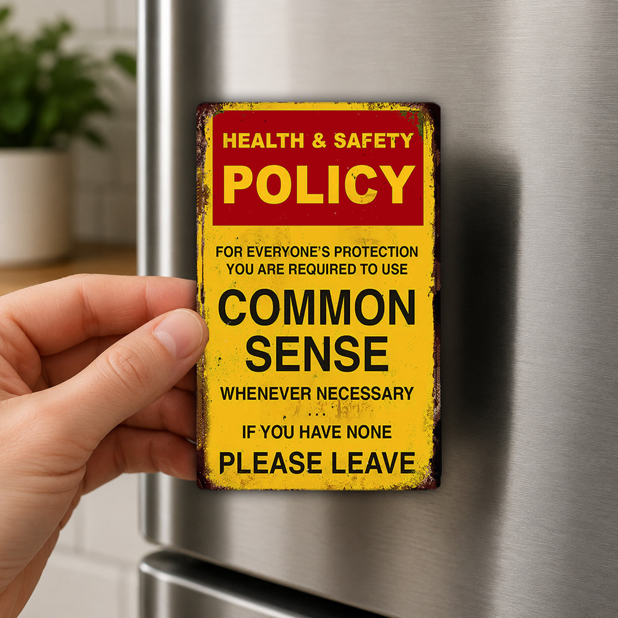 A person's hand is holding a metal sign with a red and yellow color scheme, which appears to be a warning or safety policy sign.