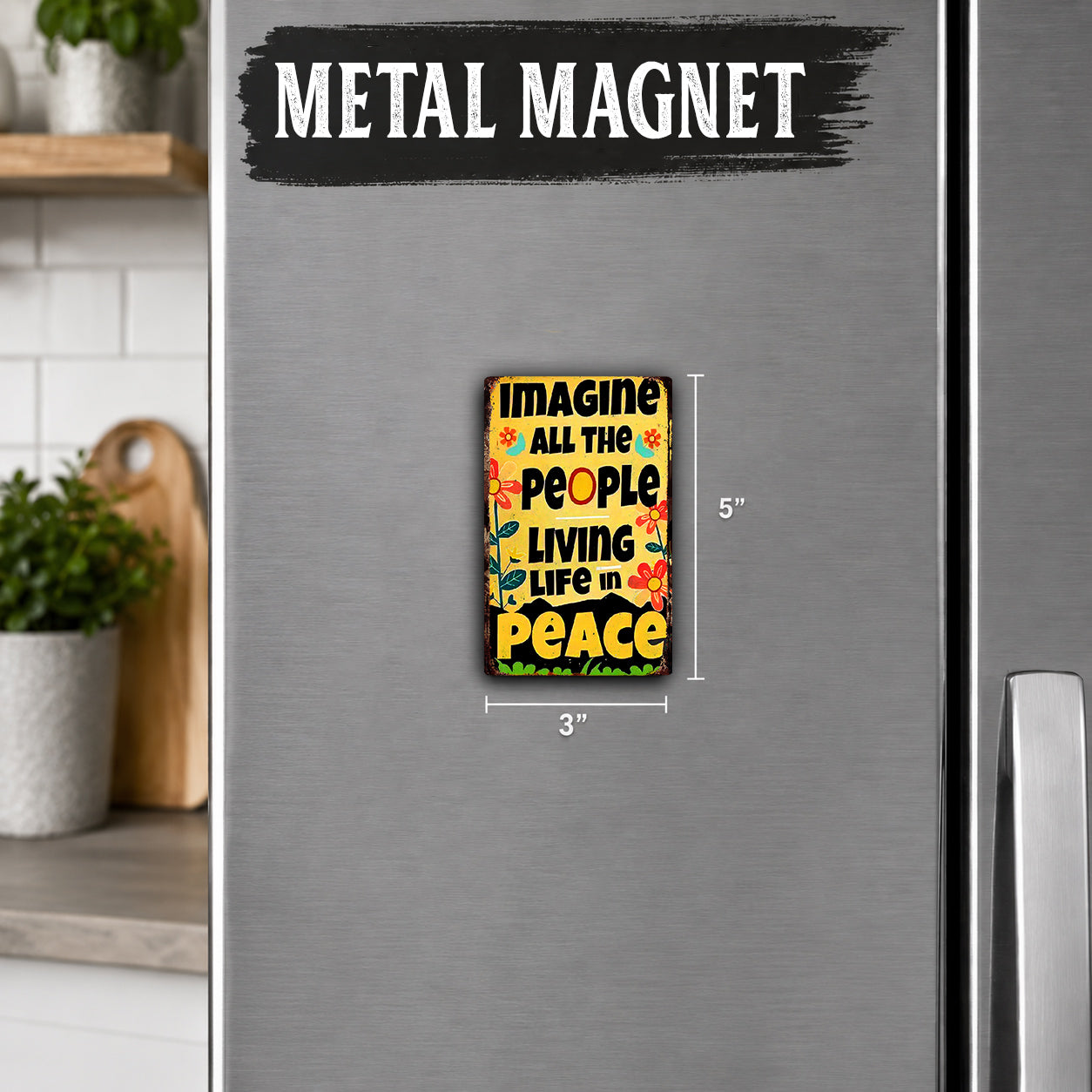 a small, colorful magnet with the text "IMAGINE ALL THE PEOPLE LIVING LIFE IN PEACE" on it. The magnet is placed on a refrigerator, and there is a wooden cutting board and a potted plant visible in the background.