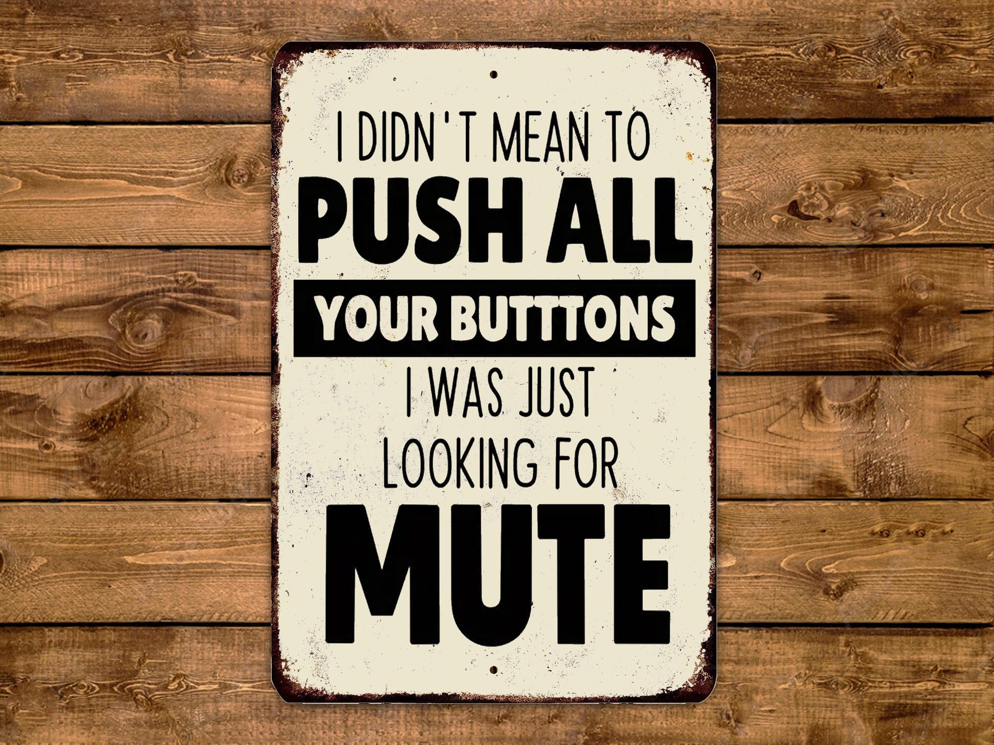 a humorous sign with the text "I DIDN'T MEAN TO PUSH ALL YOUR BUTTONS I WAS JUST LOOKING FOR MUTE" displayed on a wooden background.