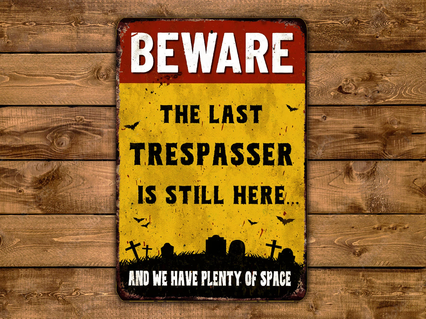 A vintage-style metal sign with the text "BEWARE THE LAST TRESPASSE IS STILL HERE AND WE HAVE PLENTY OF SPACE" displayed on a wooden background.