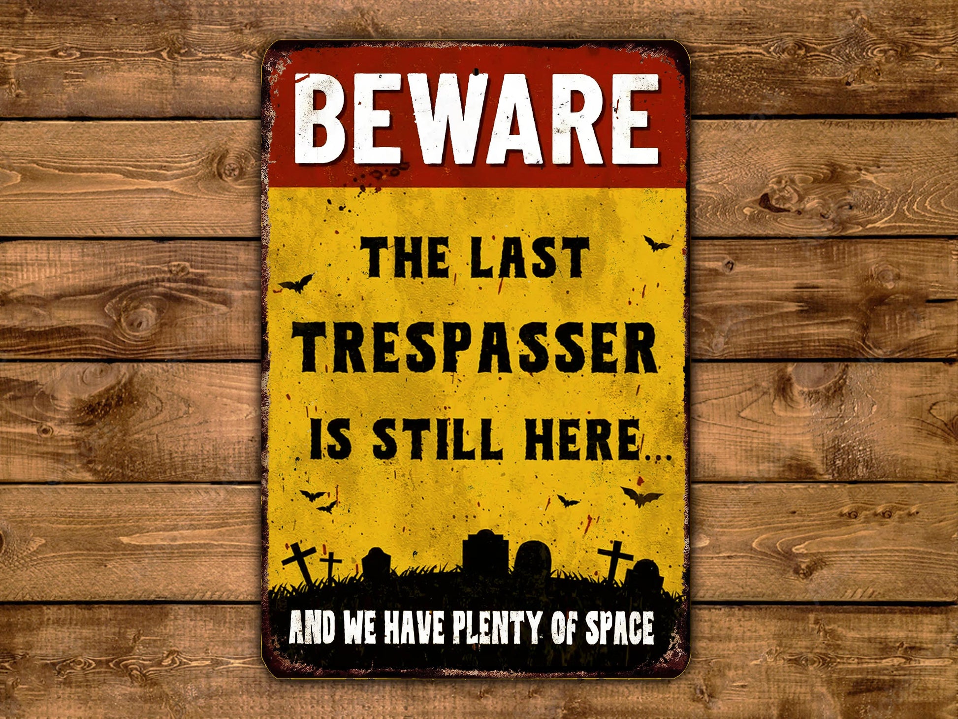 A vintage-style metal sign with the text "BEWARE THE LAST TRESPASSE IS STILL HERE AND WE HAVE PLENTY OF SPACE" displayed on a wooden background.