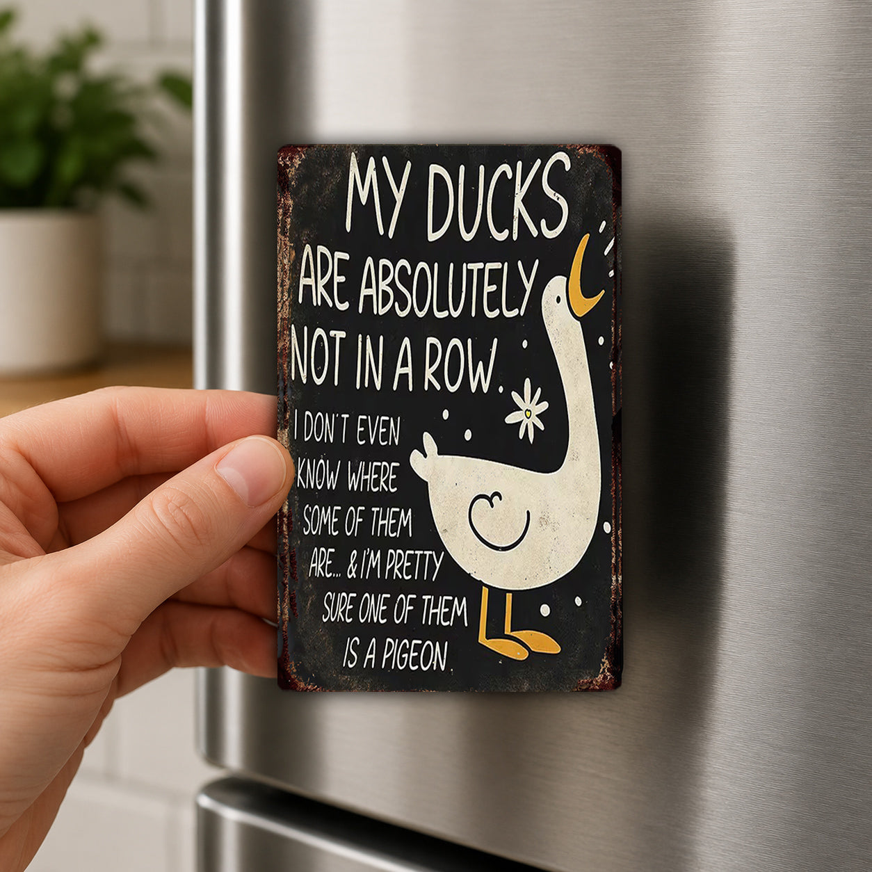 A person's hand is holding a small, vintage-style sign with a humorous message about ducks.