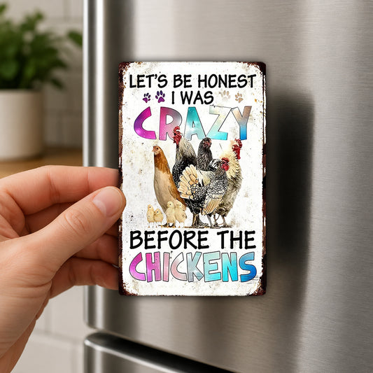 A person's hand holding a metal refrigerator magnet with a colorful design featuring chickens and text.