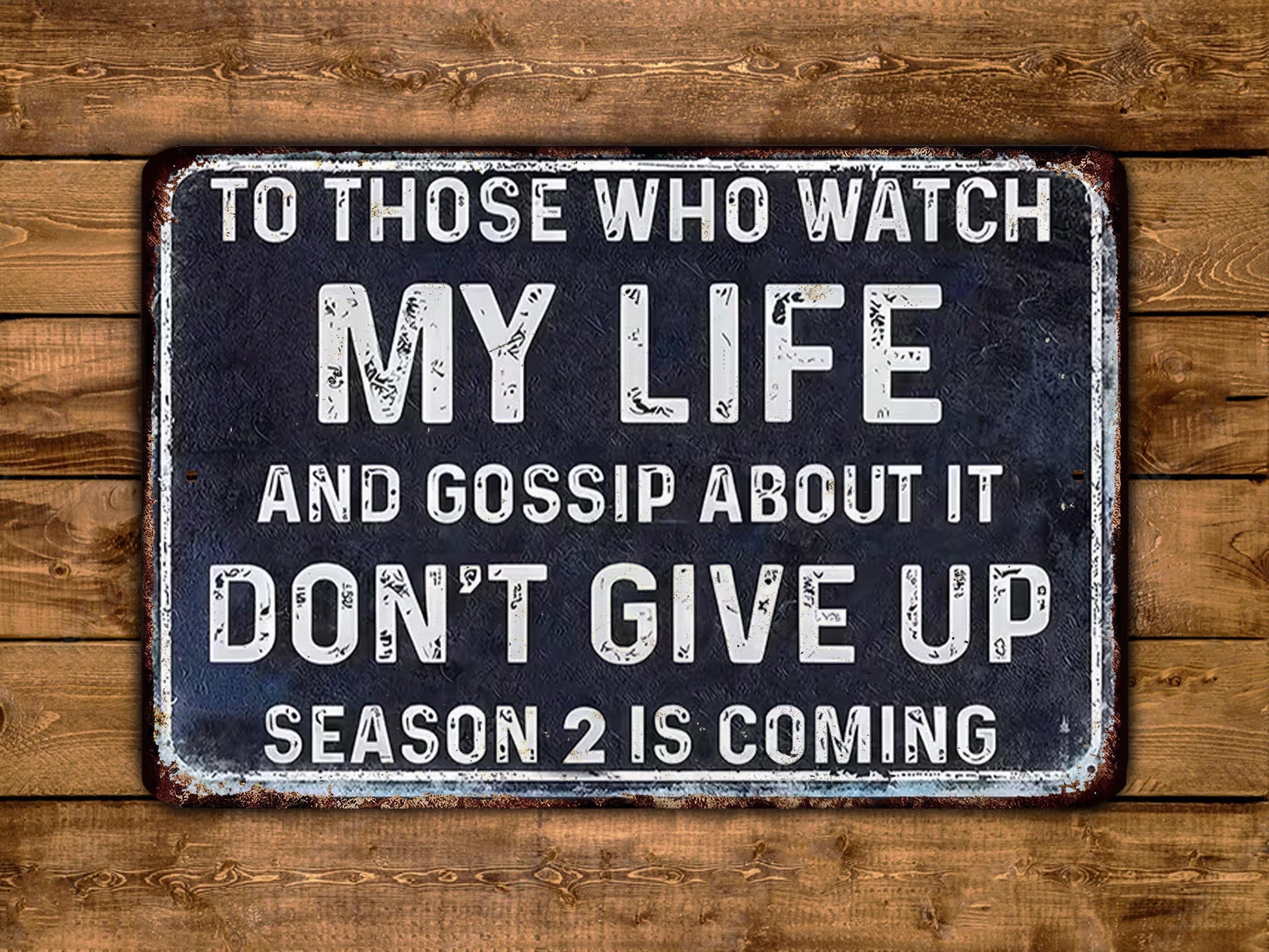 The image is a sign with the text "To those who watch my life and gossip about it, don't give up season 2 is coming" displayed on a wooden background.