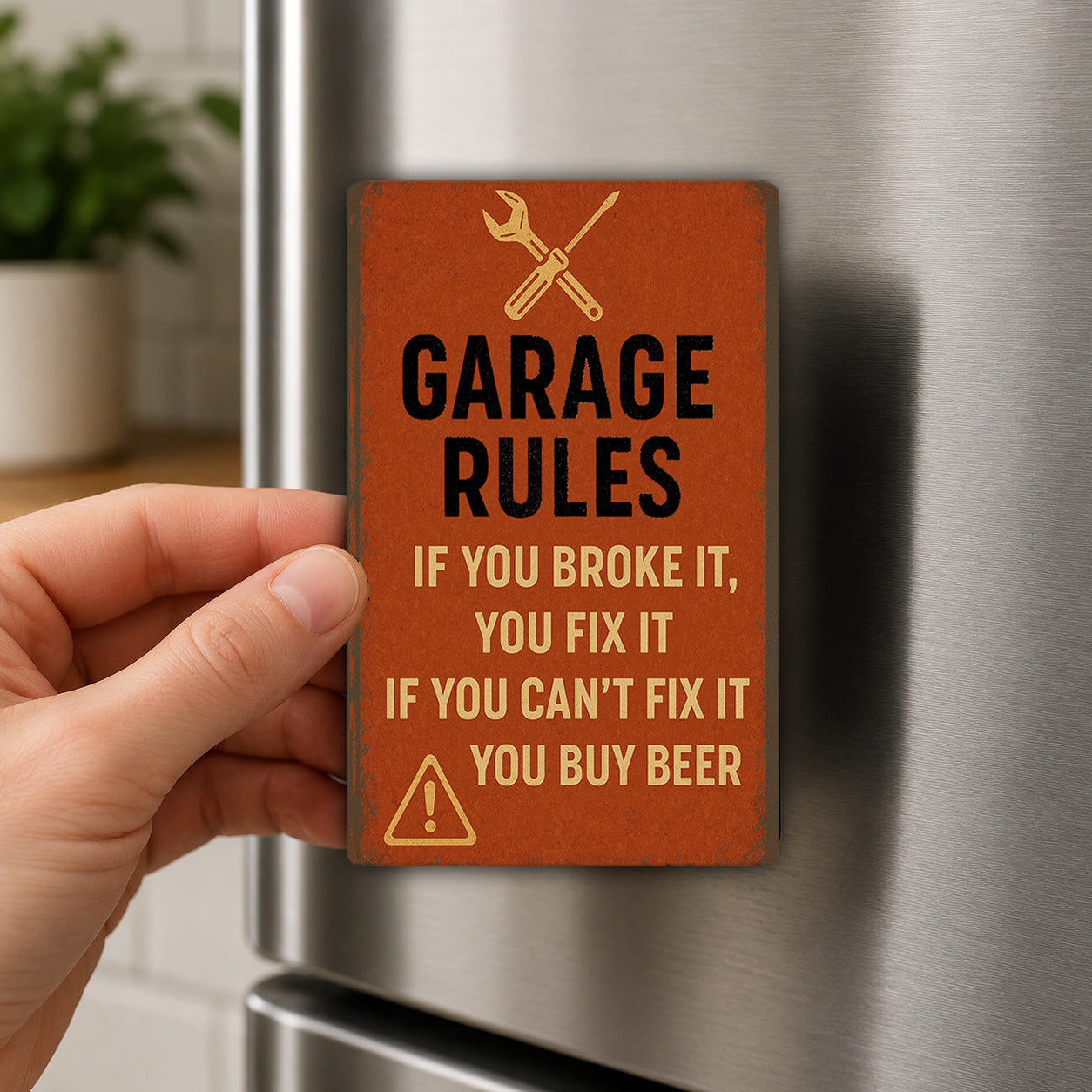 a person's hand holding a small orange sign with black text and a warning symbol, which appears to be a humorous reminder about garage rules.