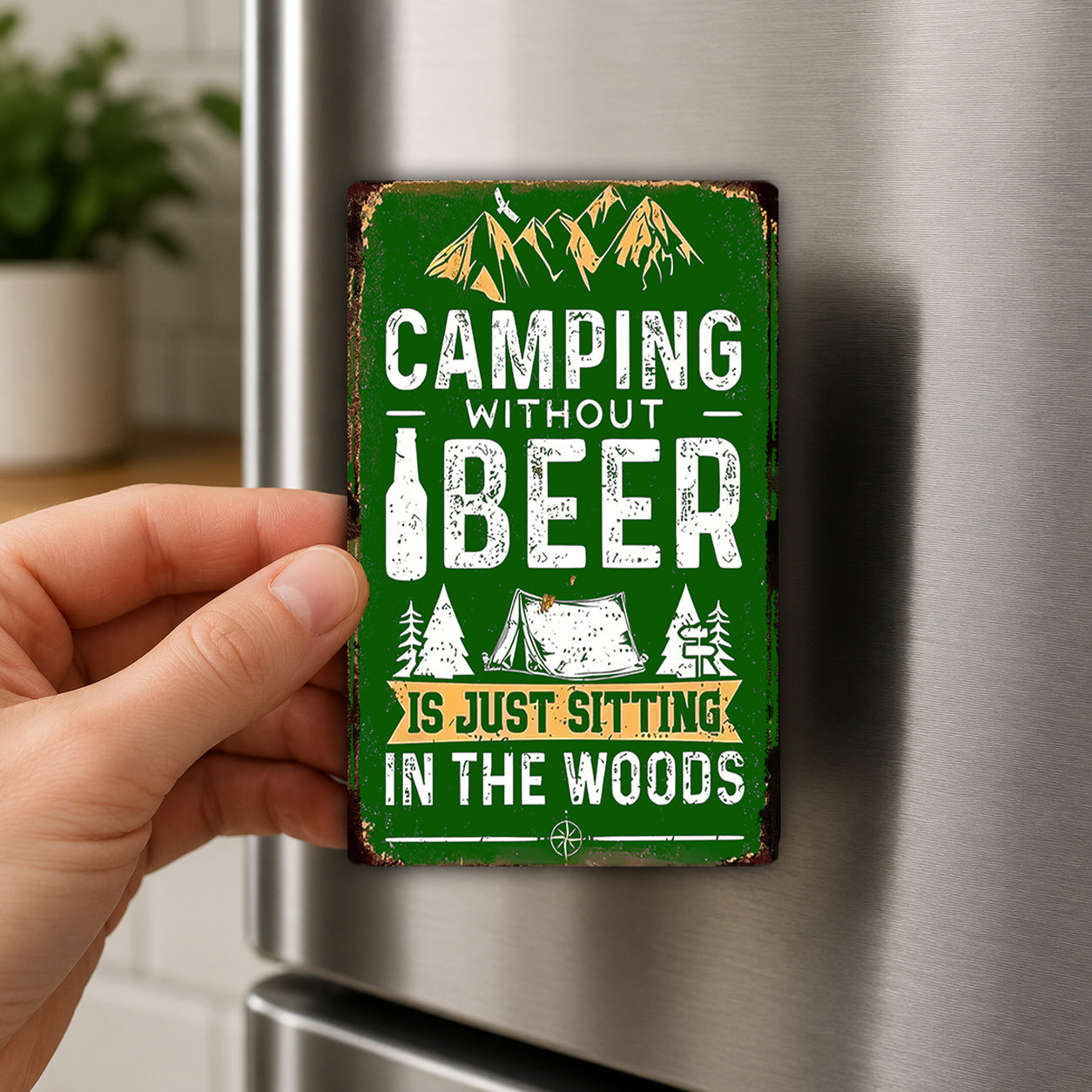 a person's hand holding a green sign with the text "Camping without beer is just sitting in the woods" against a metal background.