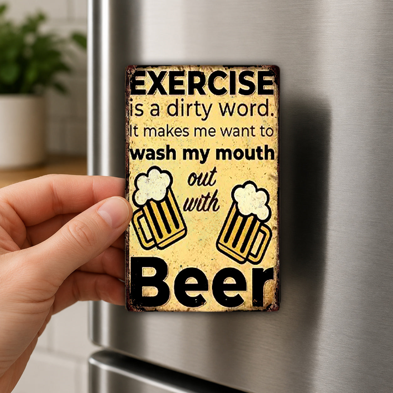 a person's hand holding a metal magnet with a humorous text and beer mug design.