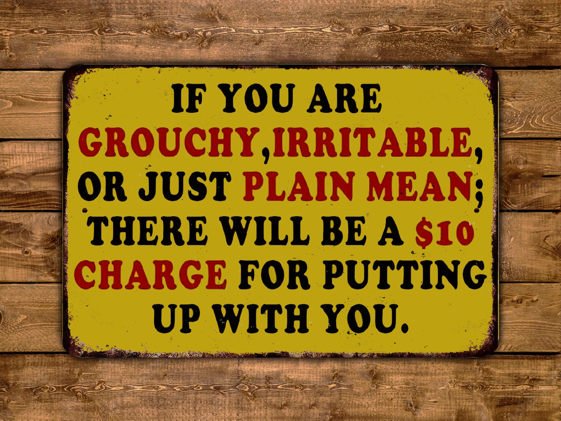 The image is a yellow sign with black text that reads "IF YOU ARE GROUCHY, IRRITABLE, OR JUST PLAIN MEAN; THERE WILL BE A $10 CHARGE FOR PUTTING UP WITH YOU."