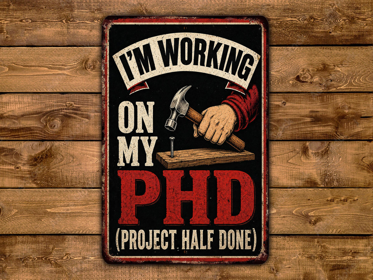 The image is a humorous sign that reads "I'm working on my PhD (project half done)" with a hammer and a wooden plank.