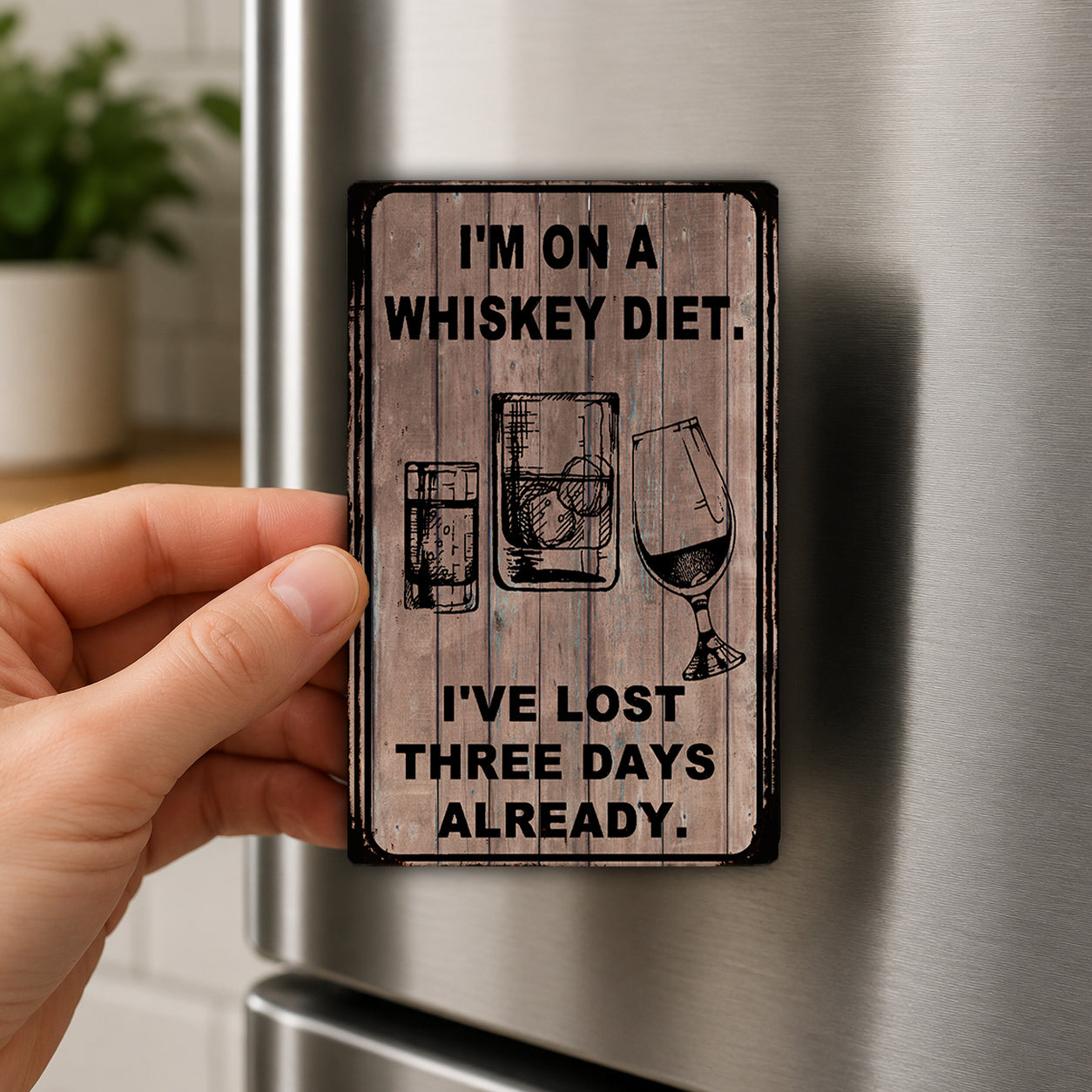 A person's hand is holding a small wooden sign with text and illustrations of alcoholic beverages, such as whiskey glasses and wine glasses.