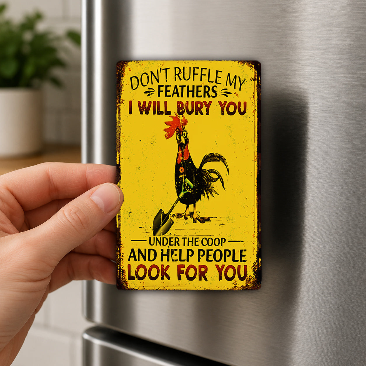 A person's hand holding a yellow metal magnet with a rooster and text on it.