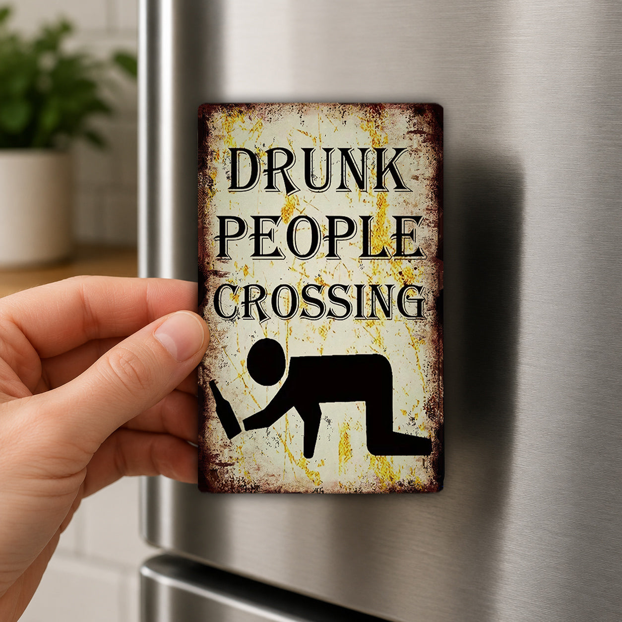A hand is holding a metal sign with the text "DRUNK PEOPLE CROSSING" and a silhouette of a person holding a beer bottle.