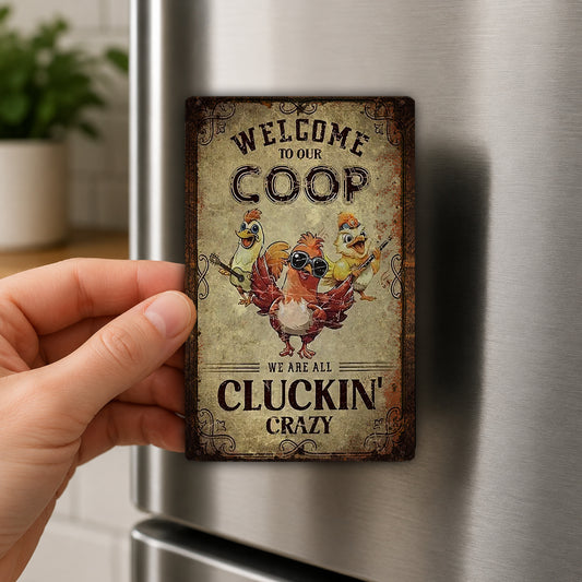 A person's hand is holding a metal refrigerator magnet with a cartoon image of three chickens and the text "Welcome to our COOP we are all CLUCKIN' CRAZY".