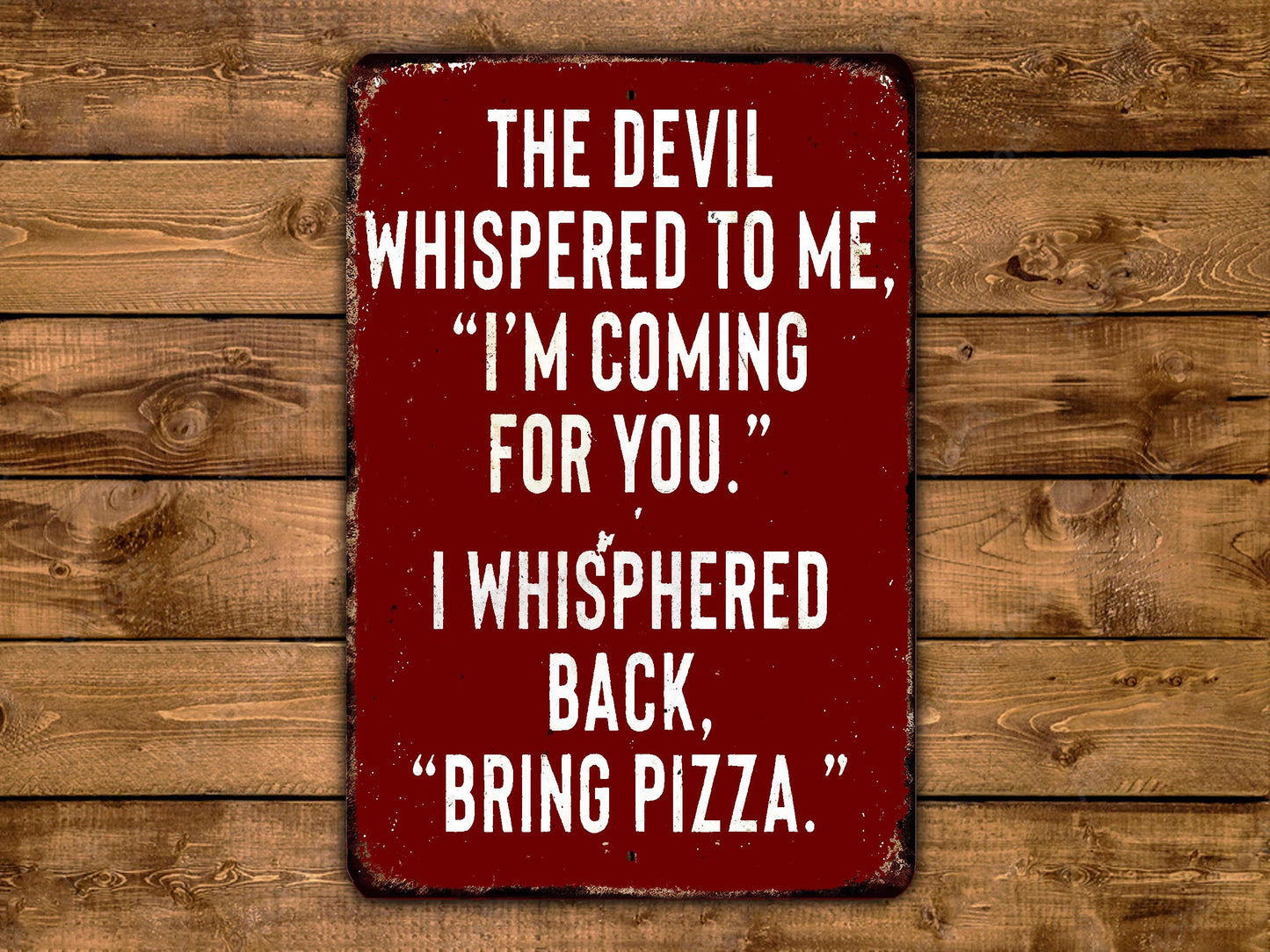 a red sign with white text that reads "THE DEVIL WHISPERED TO ME, "I'M COMING FOR YOU." I WHISPERED BACK, "BRING PIZZA."