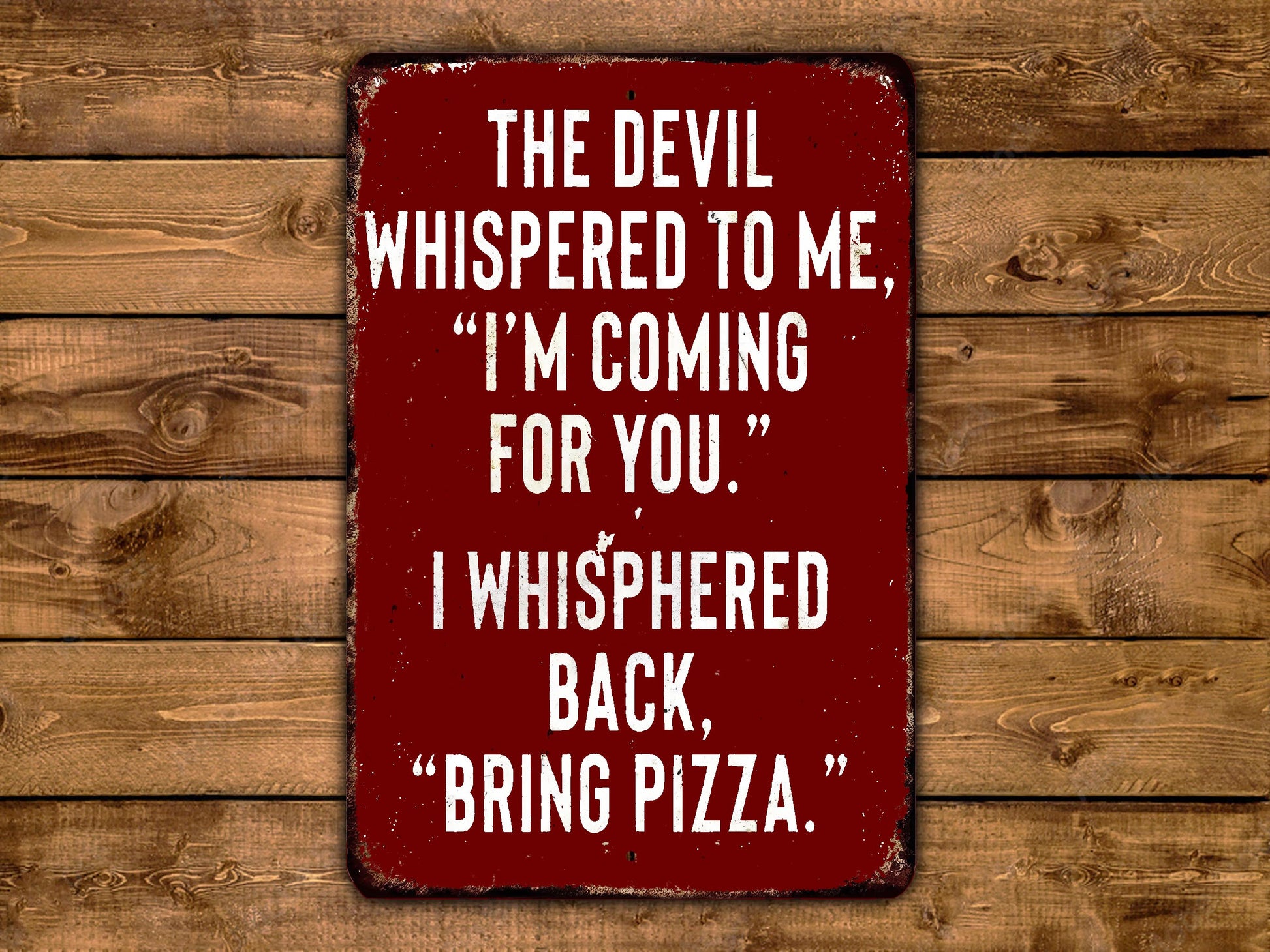 a red sign with white text that reads "THE DEVIL WHISPERED TO ME, "I'M COMING FOR YOU." I WHISPERED BACK, "BRING PIZZA."