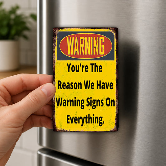 A person's hand is holding a yellow and red warning sign attached to a refrigerator.