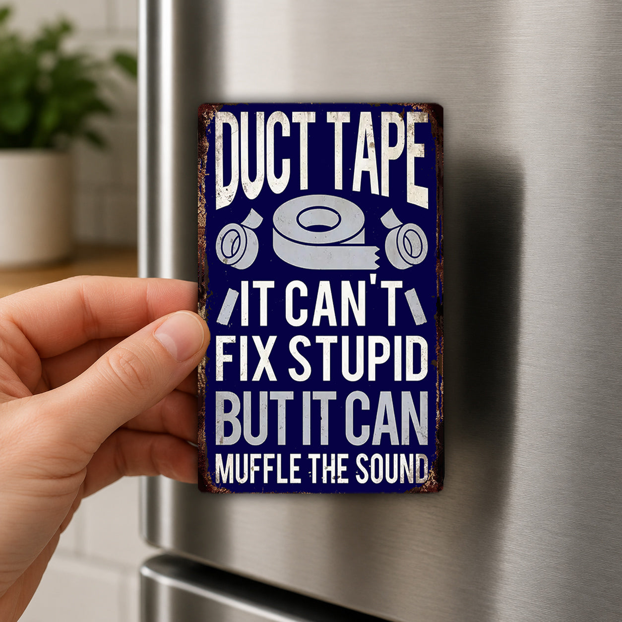 A person's hand is holding a metal sign with the text "Duct Tape It Can't Fix Stupid But It Can Muffle the Sound" on it.