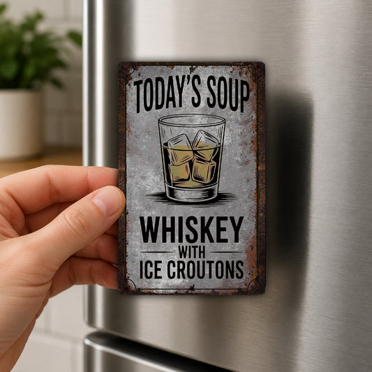 A person's hand is holding a metal sign with the text "Today's Soup Whiskey with Ice Croutons" on it.