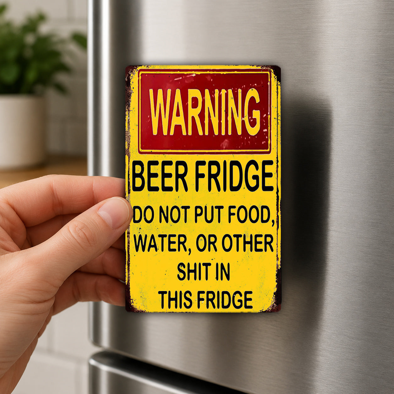 A person's hand is holding a yellow and red warning sign attached to a refrigerator.