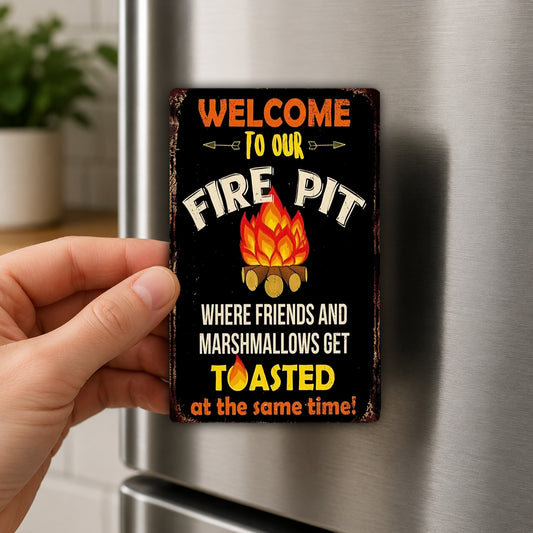 A person's hand holding a sign that says "Welcome to our fire pit" with a fire pit illustration and the text "Where friends and marshmallows get toasted at the same time!"