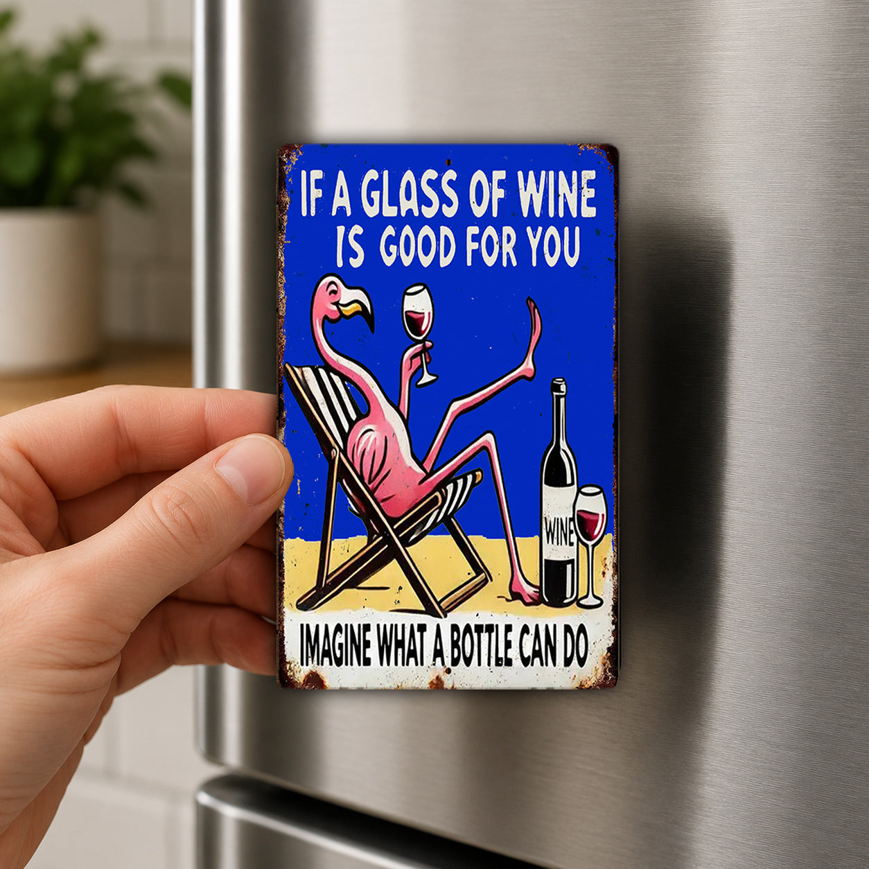 A person is holding a metal refrigerator magnet with a cartoon flamingo sitting in a beach chair and holding a glass of wine.