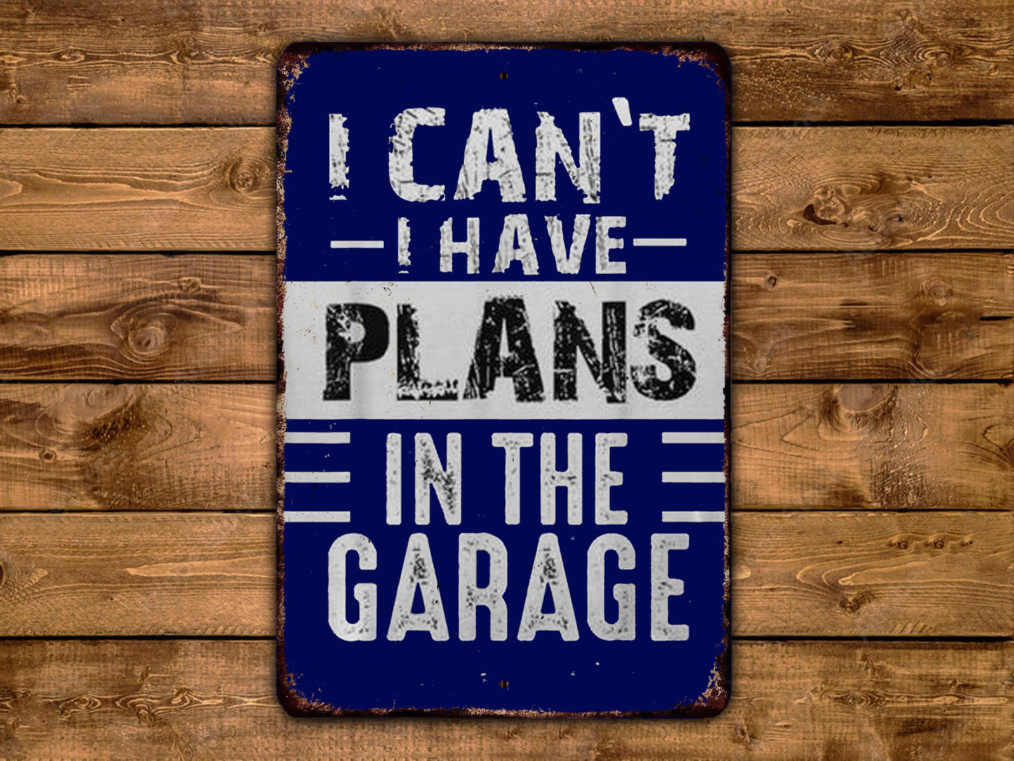 A blue and white sign with the text "I CAN'T HAVE PLANS IN THE GARAGE" displayed on a wooden background.