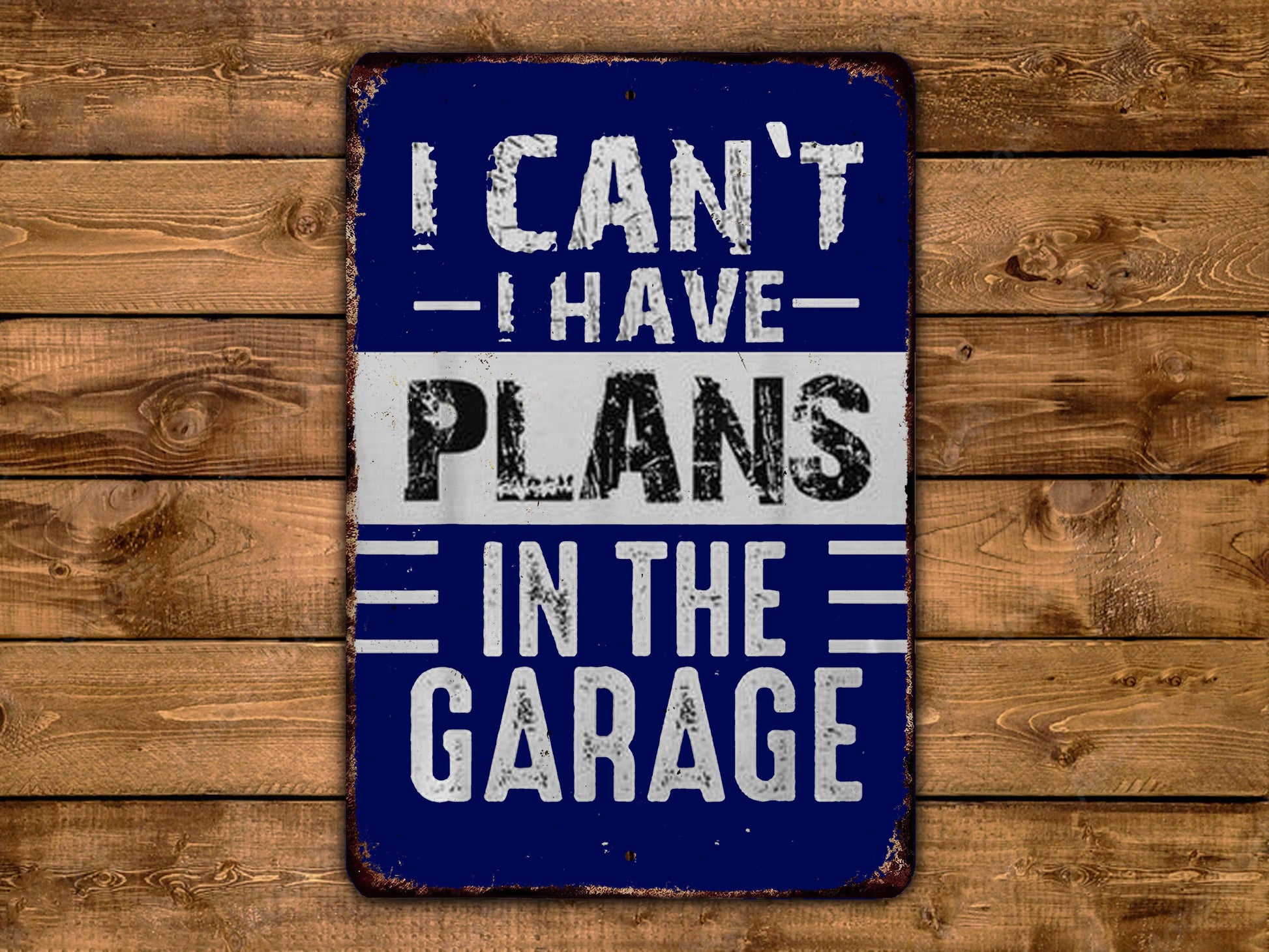 A blue and white sign with the text "I CAN'T HAVE PLANS IN THE GARAGE" displayed on a wooden background.