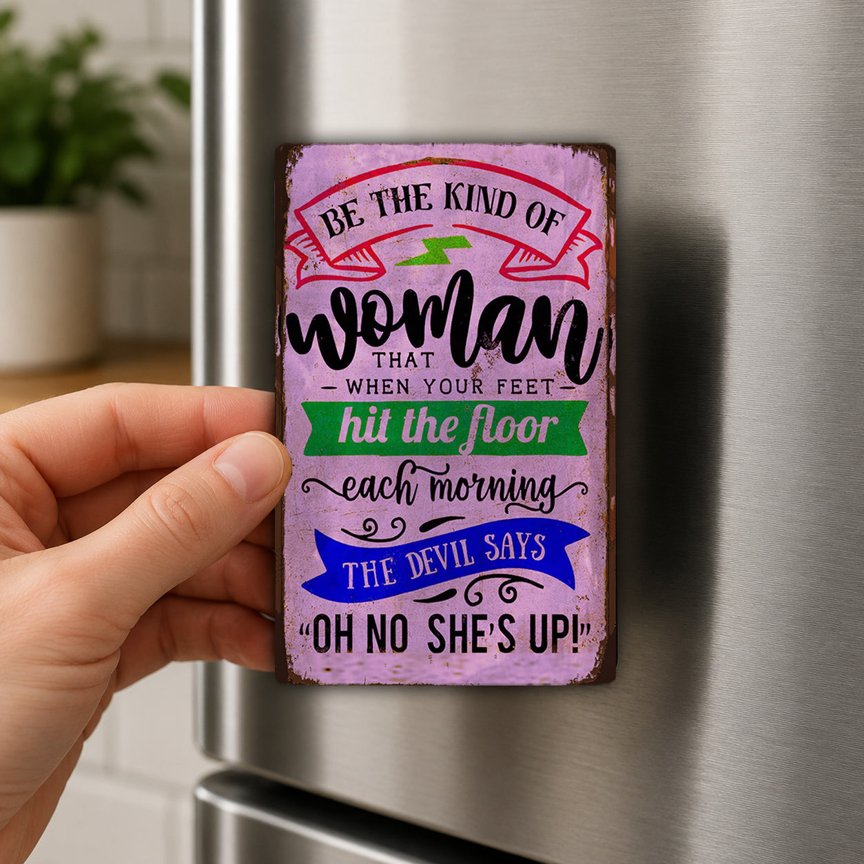 A hand holding a colorful, vintage-style sign with text on it, which appears to be a humorous or inspirational quote.