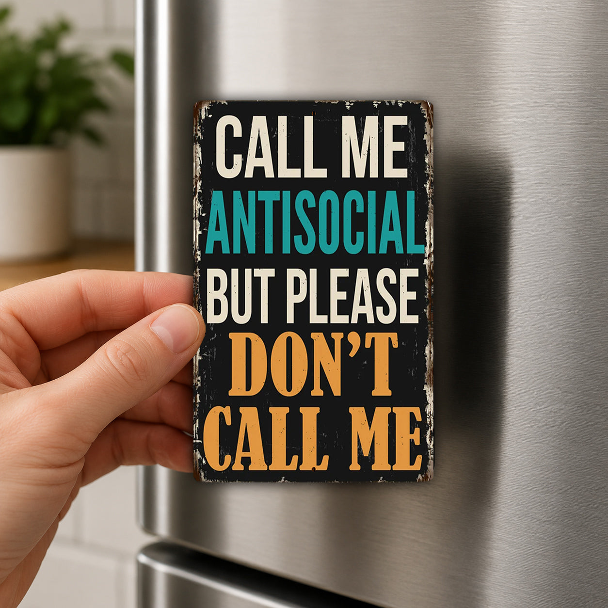A person's hand is holding a small, vintage-style sign with the text "CALL ME ANTISOCIAL BUT PLEASE DON'T CALL ME" on it.