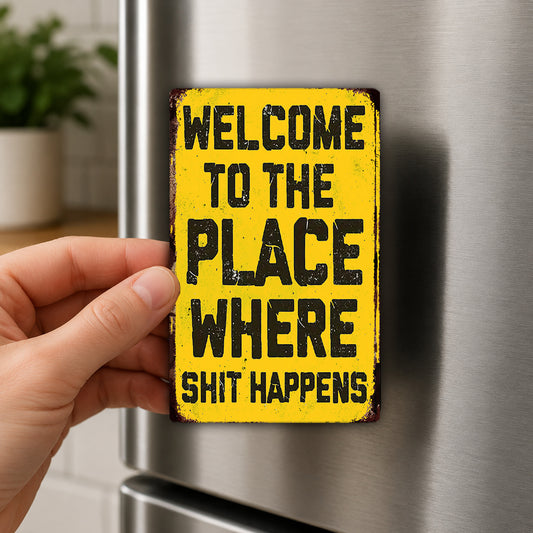 A person's hand holding a yellow sign with the text "WELCOME TO THE PLACE WHERE SHIT HAPPENS" on it.