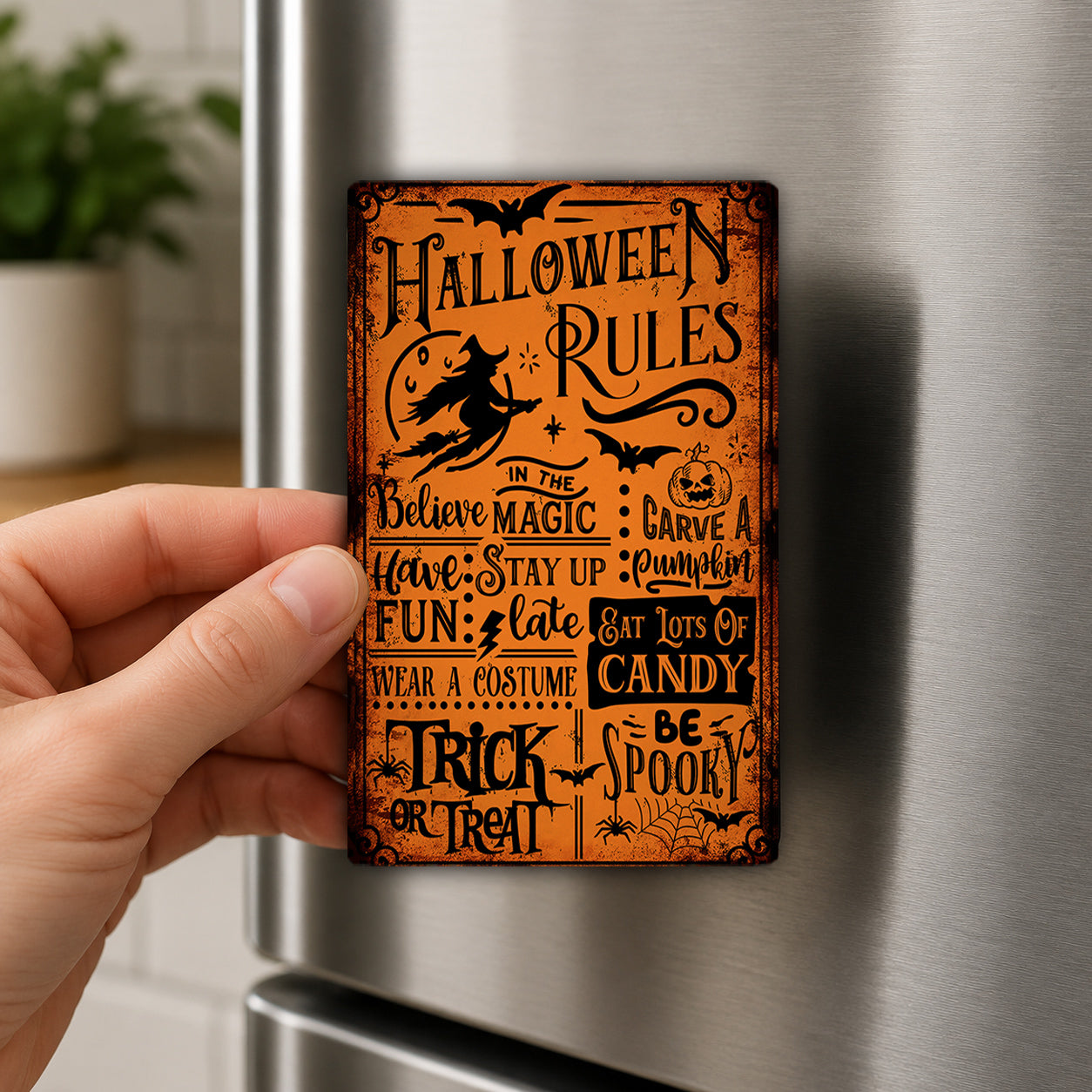 A hand is holding a Halloween-themed magnet on a refrigerator.
