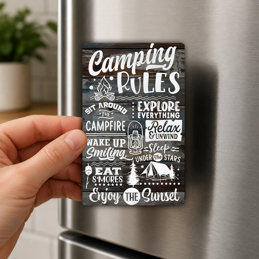 a hand holding a magnet with various camping-related phrases and illustrations on it.