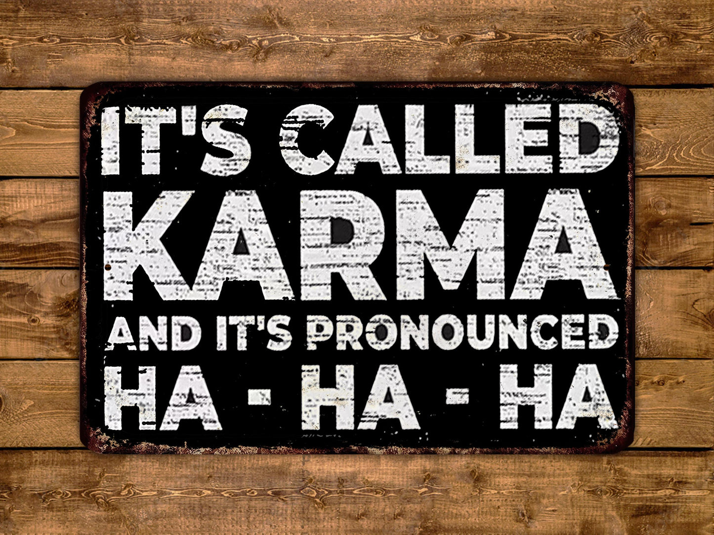 a sign with the text "It's called Karma and it's pronounced Ha-ha-ha" in a distressed, distressed font against a wooden background.