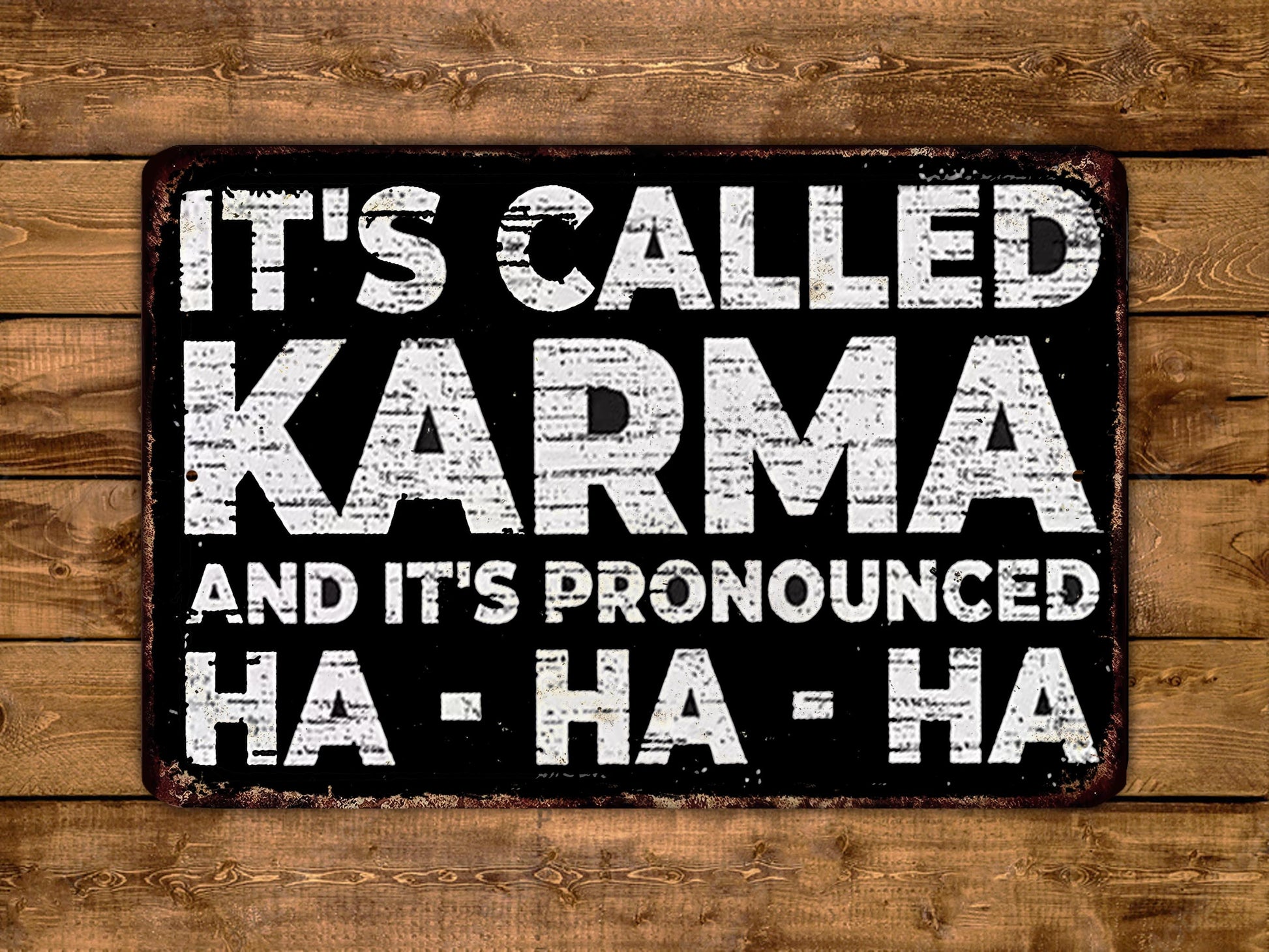 a sign with the text "It's called Karma and it's pronounced Ha-ha-ha" in a distressed, distressed font against a wooden background.