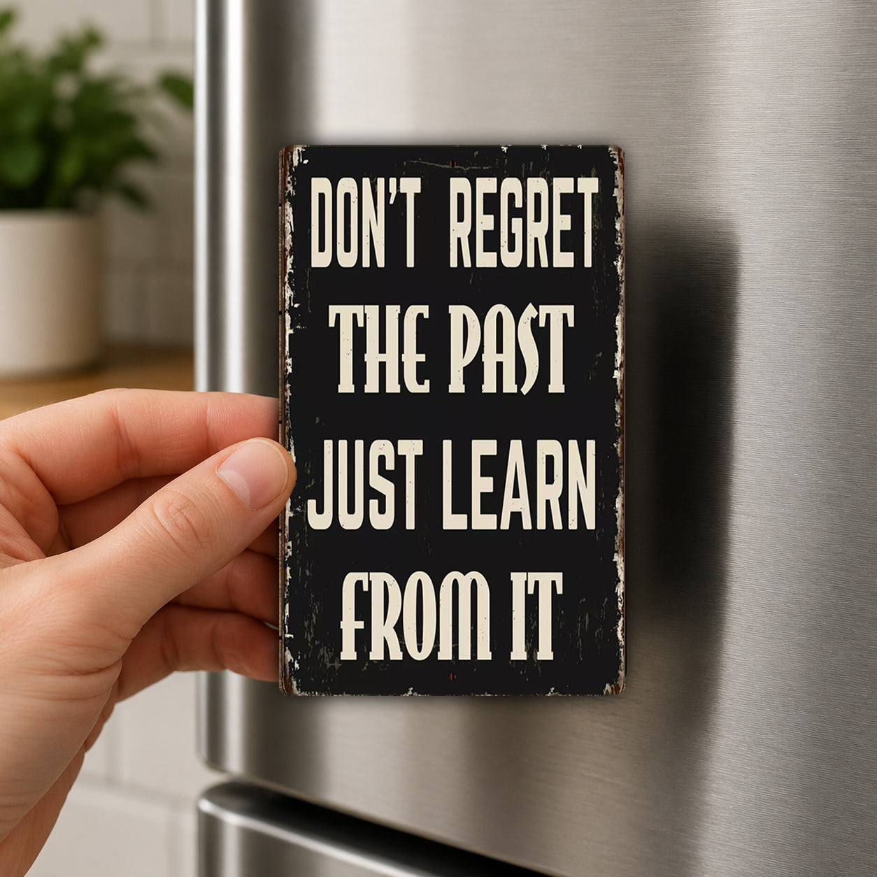 A hand holding a small sign with the text "DON'T REGRET THE PAST JUST LEARN FROM IT" on it.