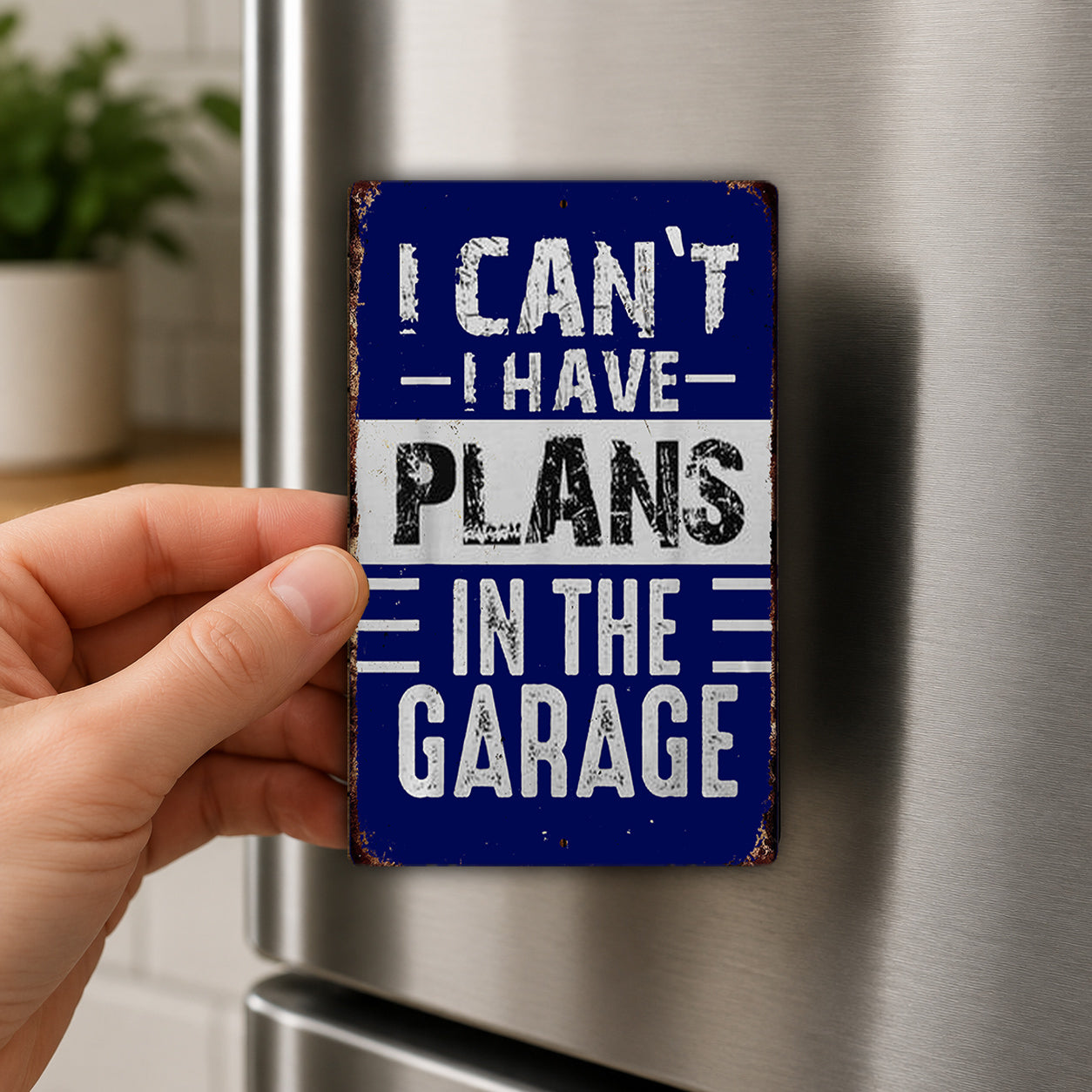 A hand is holding a blue and white sign with the text "I CAN'T HAVE PLANTS IN THE GARAGE" on it.