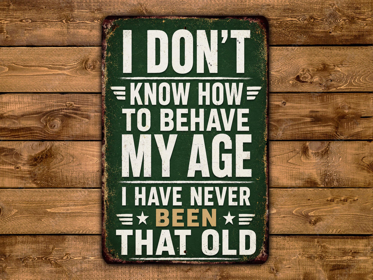 a vintage-style sign with the text "I DON'T KNOW HOW TO BEHAVE MY AGE I HAVE NEVER BEEN THAT OLD" displayed on a wooden background.