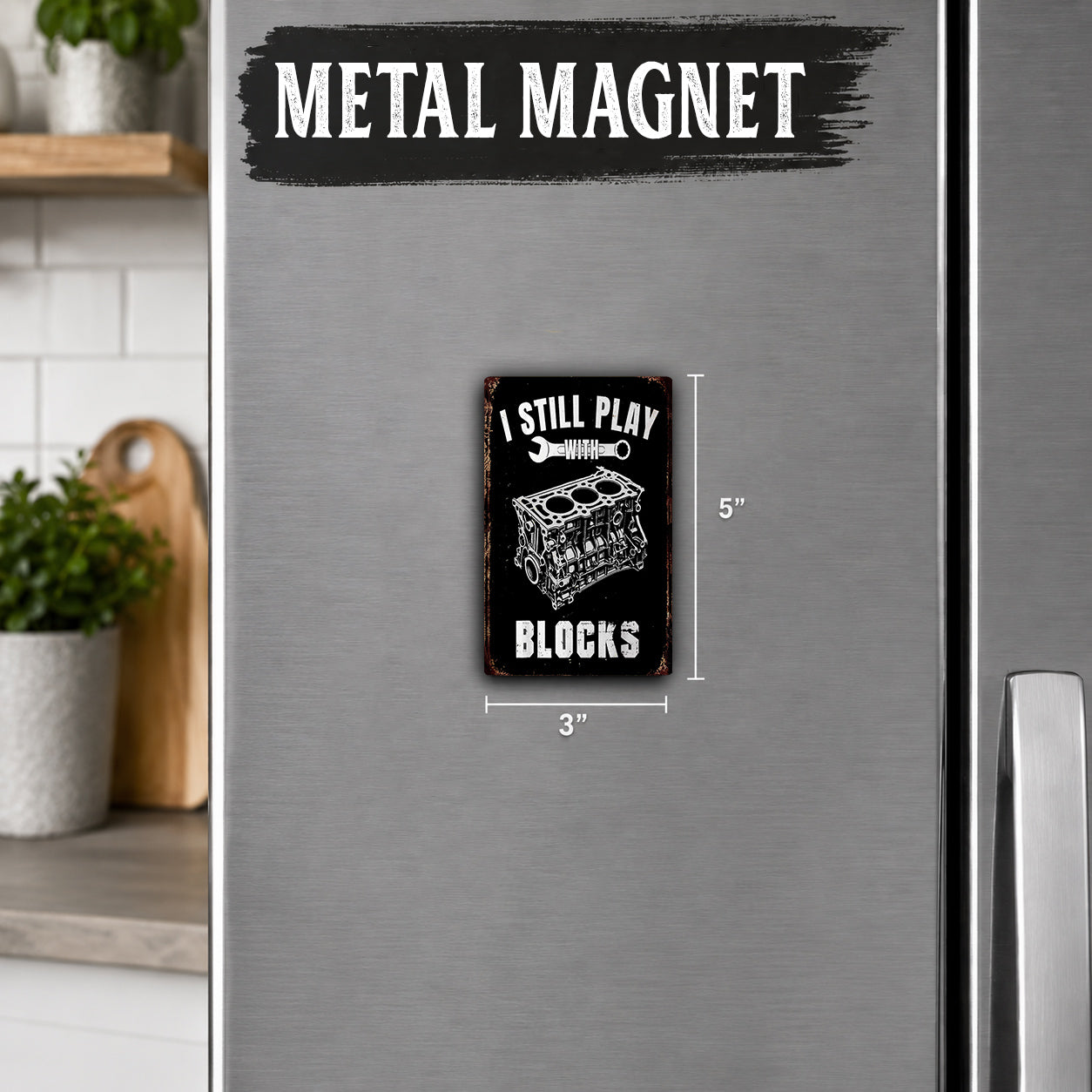 a refrigerator with a small black and white metal magnet on it. The magnet has the text "I STILL PLAY BLOCKS" and is approximately 5 inches in size.