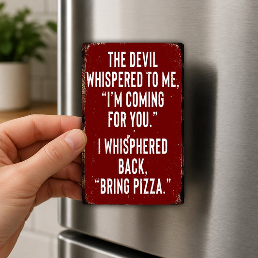 a person's hand holding a red sign with white text that reads "THE DEVIL WHISPERED TO ME, "I'M COMING FOR YOU." I WHISPERED BACK, "BRING PIZZA."