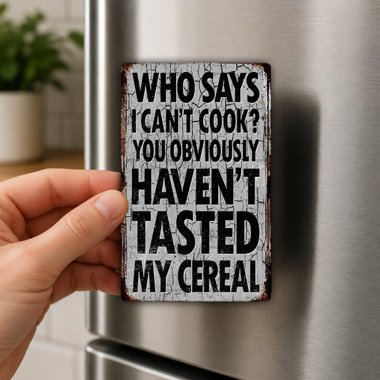 A person's hand is holding a metal sign with the text "WHO SAYS I CAN'T COOK? YOU OBVIOUSLY HAVEN'T TASTED MY CEREAL" on it.