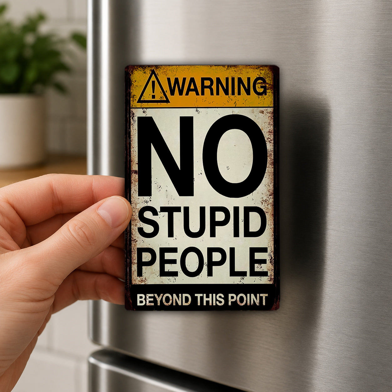 A person's hand is holding a metal sign with the text "WARNING NO STUPID PEOPLE BEYOND THIS POINT" on it.