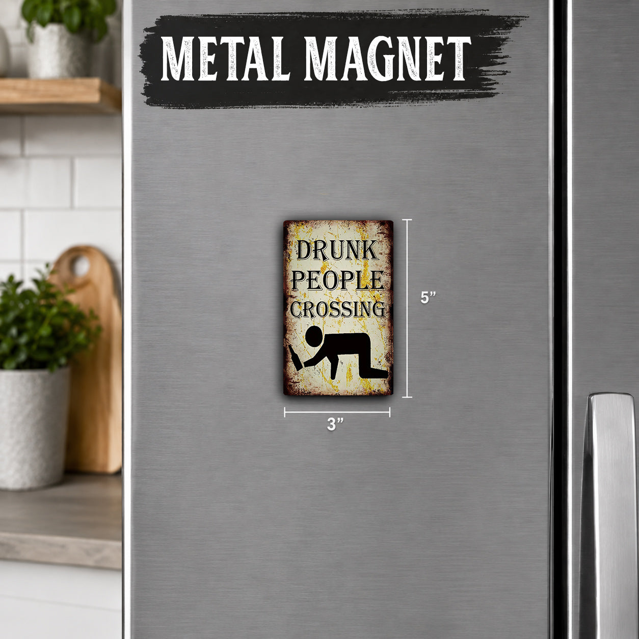 a small, vintage-style metal magnet with the text "DRUNK PEOPLE CROSSING" on it. The magnet is placed on a refrigerator, and there is a wooden cutting board visible in the background.